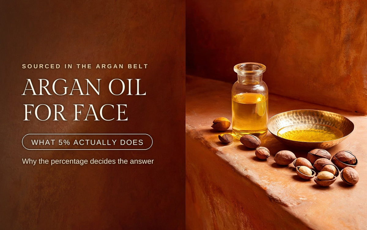 Glass vial and hammered brass dish of golden argan oil with cracked argan kernels scattered on a warm clay ledge