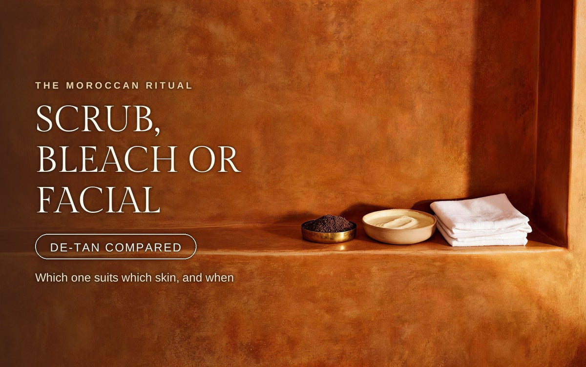 A shallow brass dish heaped with dark coarse scrub, a pale ceramic bowl of soft cream paste and a stack of folded white linen set in a row along a warm terracotta clay ledge, low raking light catching the granular texture and the metal rim